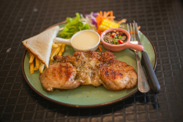 A tender pork steak with vegetables and French fries on a large plate looks very appetizing.
