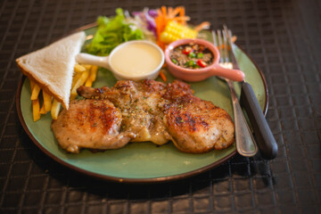 A tender pork steak with vegetables and French fries on a large plate looks very appetizing.