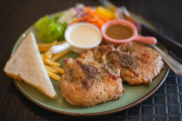 A tender pork steak with vegetables and French fries on a large plate looks very appetizing.