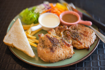 A tender pork steak with vegetables and French fries on a large plate looks very appetizing.