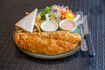 A seaside-inspired plating of tender plaice fillets coated in a light, crispy batter, accompanied by a generous heap of thin-cut fries, garnished with fresh herbs and a wedge of lemon.