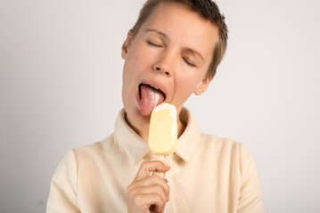 A middle-aged woman with a short haircut eats ice cream with her mouth wide open and tongue hanging out on a white background