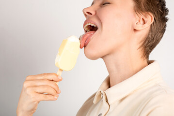 A woman with a chic cropped hairstyle relishes ice cream against a clean, white background, expressing her sweet tooth with every lick