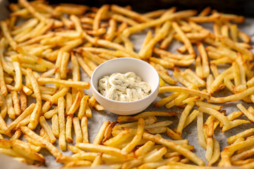 Freshly prepared French fries lying in front of the oven and sauce for them with herbs