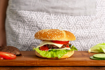 Homemade large hamburger with buns covered with sesame seeds, fresh green salad, cheese, tomatoes and beef patty