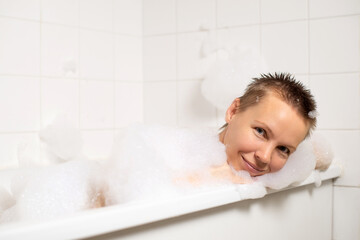 In the warm bubble-filled tub, a middle-aged woman relaxes. Happiness shines through her face