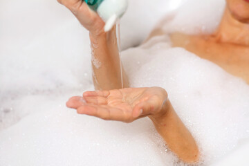 A woman takes a bath with foam. She pours gel onto her palm in the shower