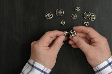 A male tailor holds sewing buttons made of metal in his hands. Decorative buttons of silver color. Hands and sewing accessories are on the surface of the table in dark brown color.