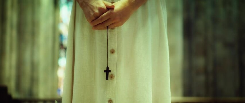 Woman praying in the church. Adult girl parishioner holding a religious wooden cross in hands.