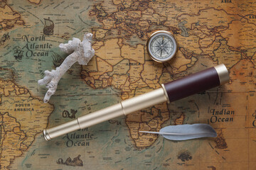 Spyglass, a compass, a branch of coral and a bird's feather - a symbol of travelers lie on an old map. View from above