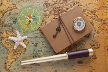 Spyglass, a compass, a starfish and a leather-bound book lie on an old map. View from above