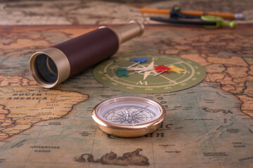 Brass compass, a spyglass, a pencil with a compass and multi-colored markers lie on an old map. Close-up