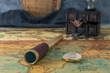 Spyglass and a compass lie on an old map against the background of a forged chest with coins. Close-up