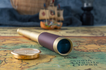 Spyglass and a compass lie on an old map against the background of a model of a wooden sailboat. Close-up