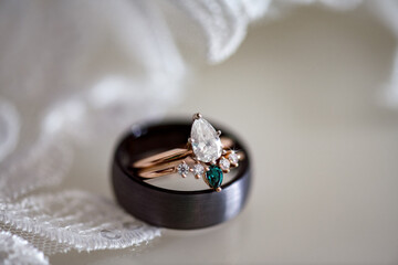 bridal ring set with rose gold, marquis shaped diamonds and emeralds resting inside a black men's...