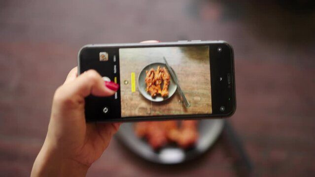 POV shot of woman taking photo of delicious chicken feet food with phone