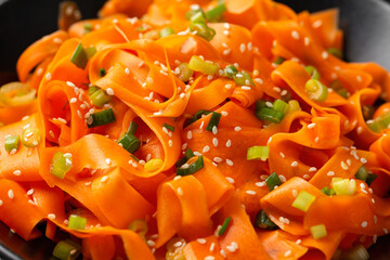 Asian carrot salad with spices and herbs in black bowl.