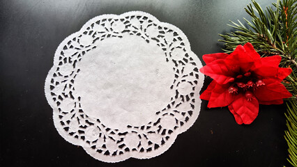 Black frame, white round napkin, green pine branch, red flower on background with reflections and sparkle of light. Abstract location for photo shoot. Cchristmas table decor. Concept of winter holiday
