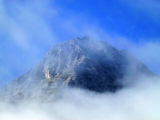 The peak of the mountain is covered with a cloud against the background of the blue sky. Beautiful natural landscape