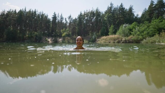 young tanned sexy woman on summer vacation or holiday swimming in alpine mountain lake, standing up from cold fresh clean water to get refreshed in heat, natural outdoor lifestyle