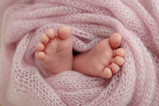 Close-up of tiny, cute, bare toes, heels and feet of a newborn girl, boy. Baby foot on pink soft coverlet, blanket. Detail of a newborn baby legs. Macro horizontal professional studio photo. 