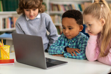 Three diverse kids exploring on laptop in classroom