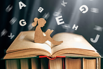 girl with dyslexia holds a book. Flying tangled letters in the air. The child learns to speak and read correctly - obrazy, fototapety, plakaty
