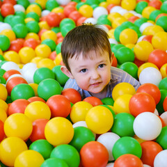 Fototapeta na wymiar Toddler baby plays in the pool with balls. Child boy crawling in the pool with plastic balls. Kid age one year nine months