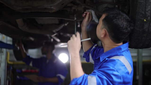 The mechanic is inspecting the car's underbody and suspension for repairs. Auto mechanics are checking the engine's operation and repairing the car's suspension.