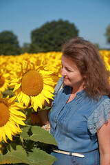 Portrait of a young woman looking at a sunflower in a sunflower field.