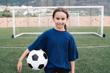 Kid girl soccer player holding ball with football field on background - Children sport life style