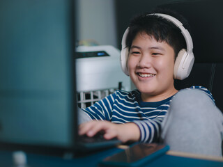 Lifestyle Asian little boys smile use desktop PCs computer to play professional video games with headphones in the house, Chat with friends, and Entertainment