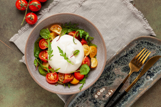 Salad with traditional italian buratta cheese with cherry tomatoes  and arugula leaves in bowl on the table. Top view