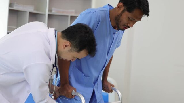 Doctor in a hospital is helping a male patient with weak leg muscles learn to walk with a cane. Physiotherapist doing physiotherapy for man practicing walking in the hospital room.