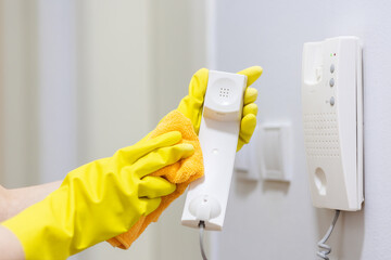 Housewife in yellow rubber gloves wipes telephone receiver. Hands close-up. Cleaning and household chores - obrazy, fototapety, plakaty