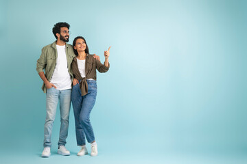 Loving young eastern couple pointing at copy space, colored background