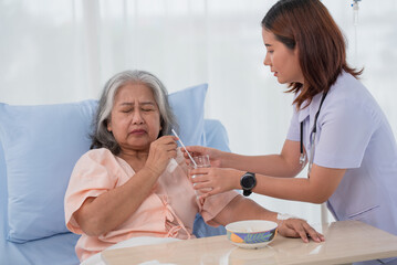 Obraz na płótnie Canvas Asian nurse helping elderly woman patient to drink on bed at hospital ward