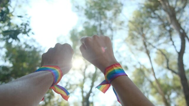 A hand and fist in the air wearing an LGBT rainbow bracelet. Pride, equality, acceptance concept. Fist raised under the sunny sky. Inclusion, diversity, unity