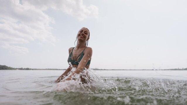 beautiful joyful young sexy girl in green swimsuit having fun in lake water and splashing water by hands. Sporty body of beautiful woman in bikini on beach tropical background