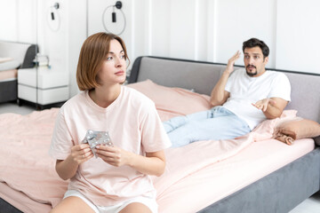 Frustrated and depressed woman sitting on the edge of the bed and holding pack of pills after conflict with her husband because of his erectile dysfunction problem