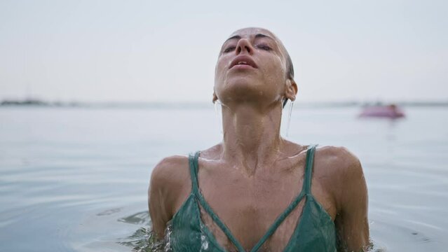 Attractive woman in green bikini emerges from water in a sea water on sunset. Pretty wet smiling girl wearing swimsuit and looks to the camera. Slow motion. relax and leisure outdoors