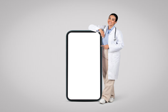 Latin woman doctor by huge cellphone with blank screen., mockup
