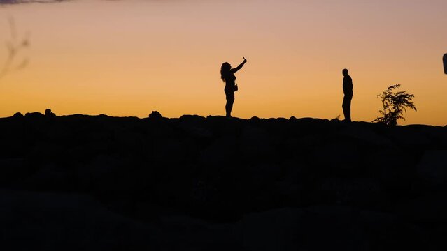 Female silhoutte takes a selfie on mobile phone at sunset. Happy woman using smartphone to take pictures of sun going down at twilight