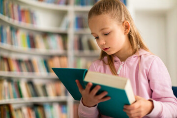 Engaged schoolgirl browsing through a book in library