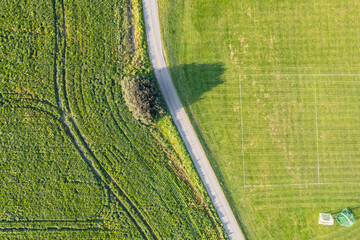 Aerial top view of green agriculture filed and football pitch, separated by a road