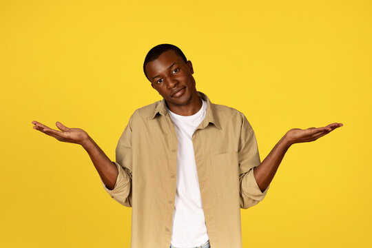 Confused calm millennial african american guy in casual spreads arms sides, hold empty space
