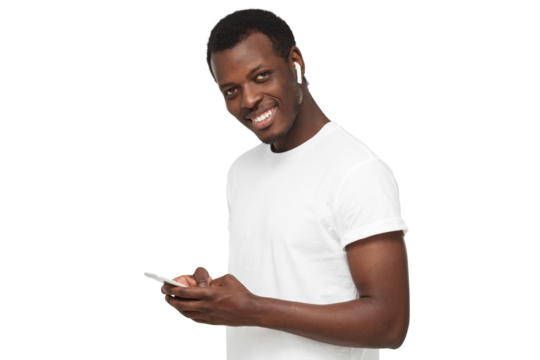 Young african american man looking and smiling at the camera, using mobile phone, listening to music with white wireless earphones