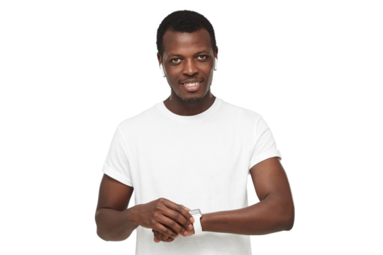 Young african american man looking at camera, checking smartwatch, wearing wireless earphones and blank white t-shirt