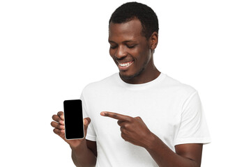 Handsome african american man in white t-shirt showing phone and pointing with finger at blank...
