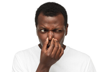 Bad smell. African american man holding his nose as if smelling something rotten and stinky looking...
